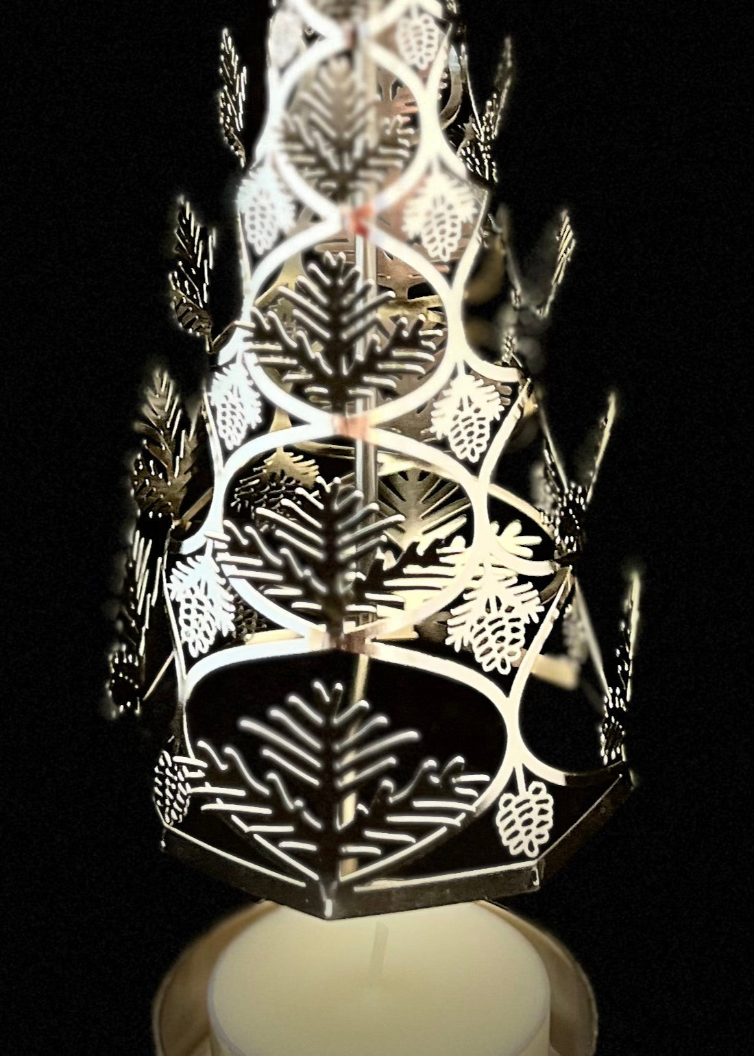 Decorative candle holder with cut-out leaf patterns on a black background