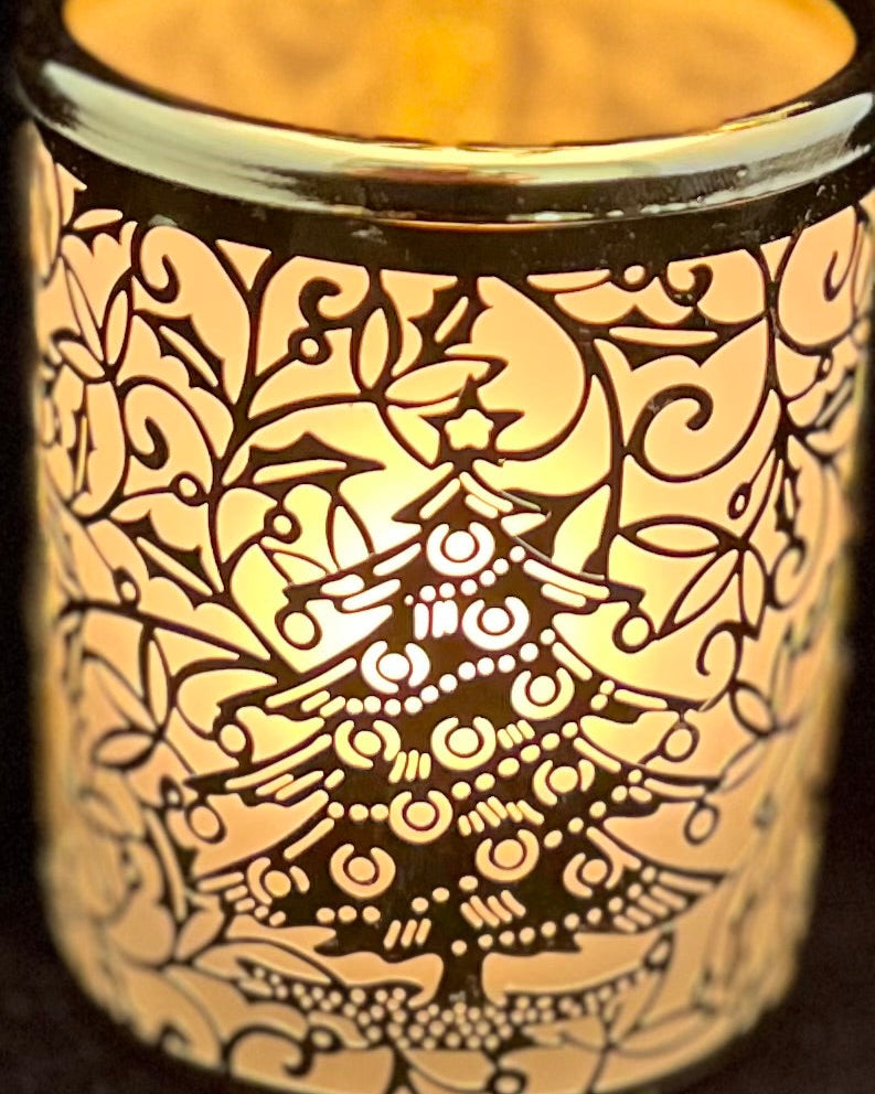 Decorative candle holder with intricate patterns and a Christmas tree design, illuminated from within.