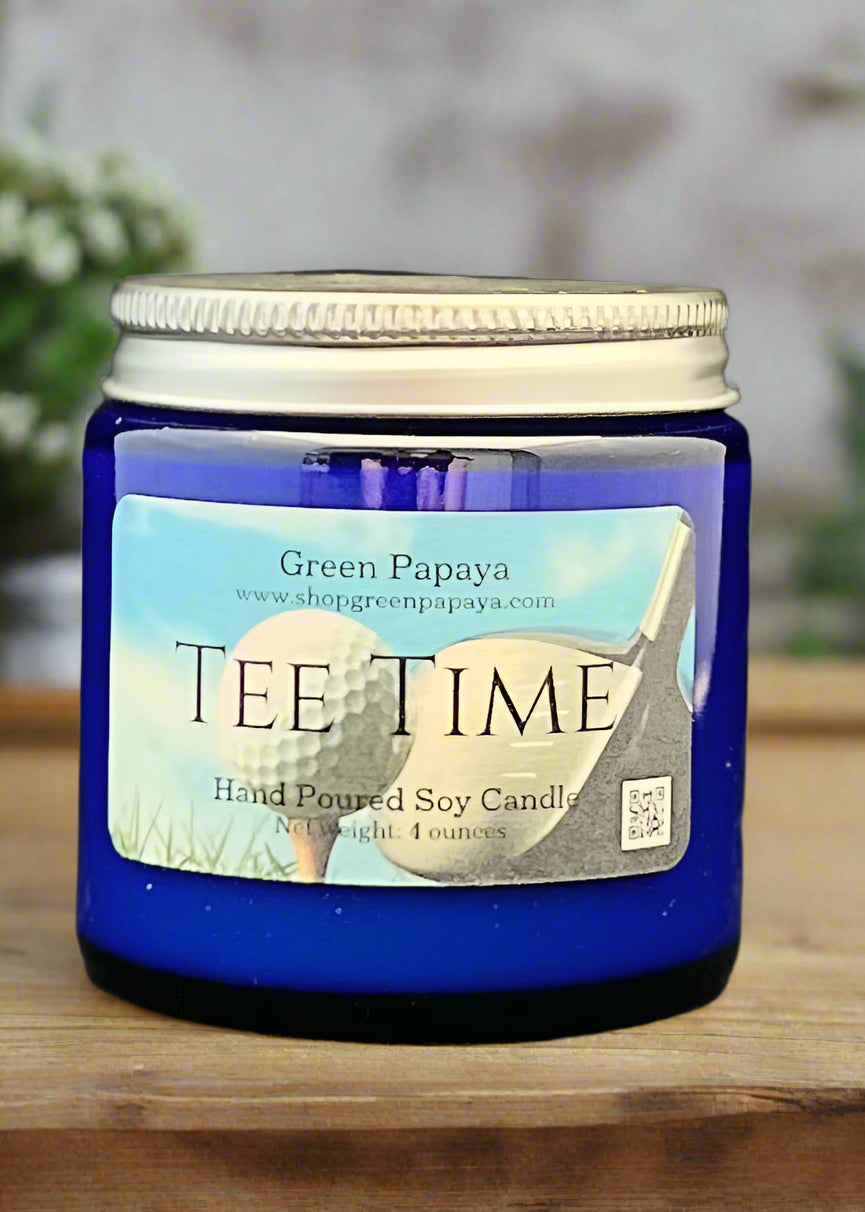Blue candle jar labeled 'Tee Time' with a visible brand label on a dark background