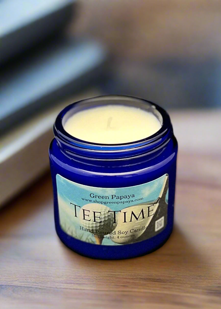 Blue candle jar labeled 'Tee Time' with a white candle inside on a dark background