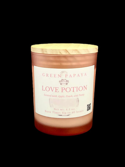 A jar candle labeled 'Green Papaya Love Potion' with a light wood lid, set against a solid black background.