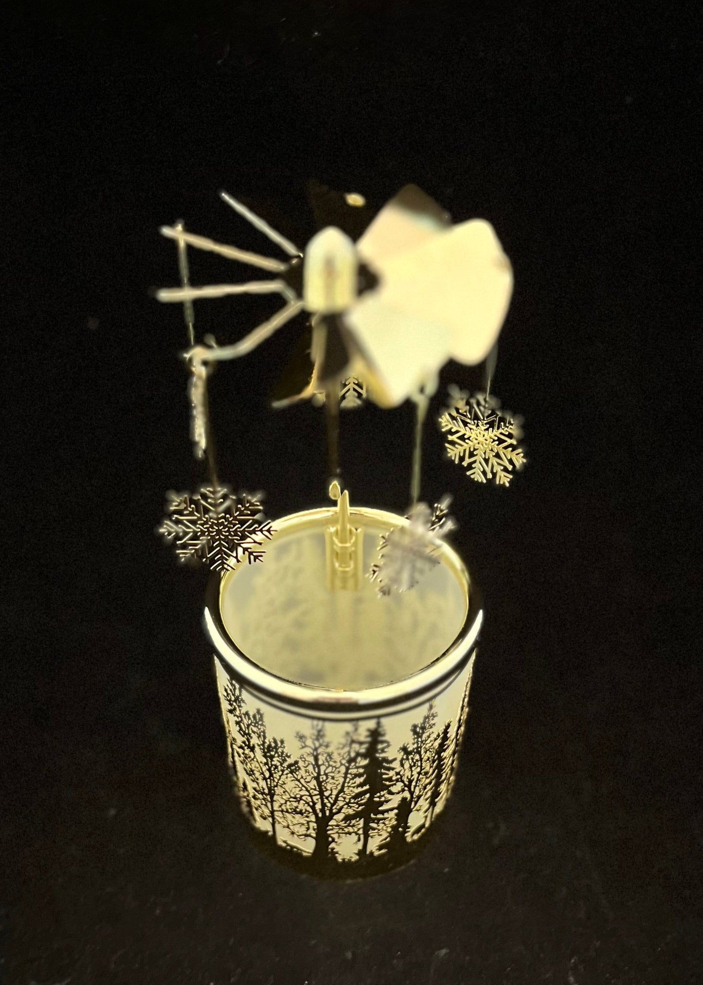 A small decorative wind spinner set in a cup with a forest pattern, photographed against a solid black background.