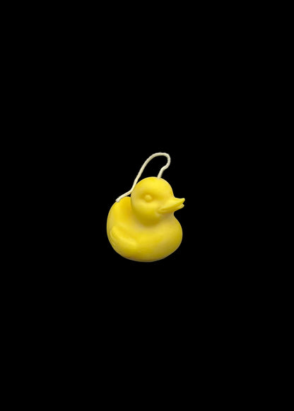 A small yellow duck-shaped candle with a white hanging loop, photographed against a dark black background.