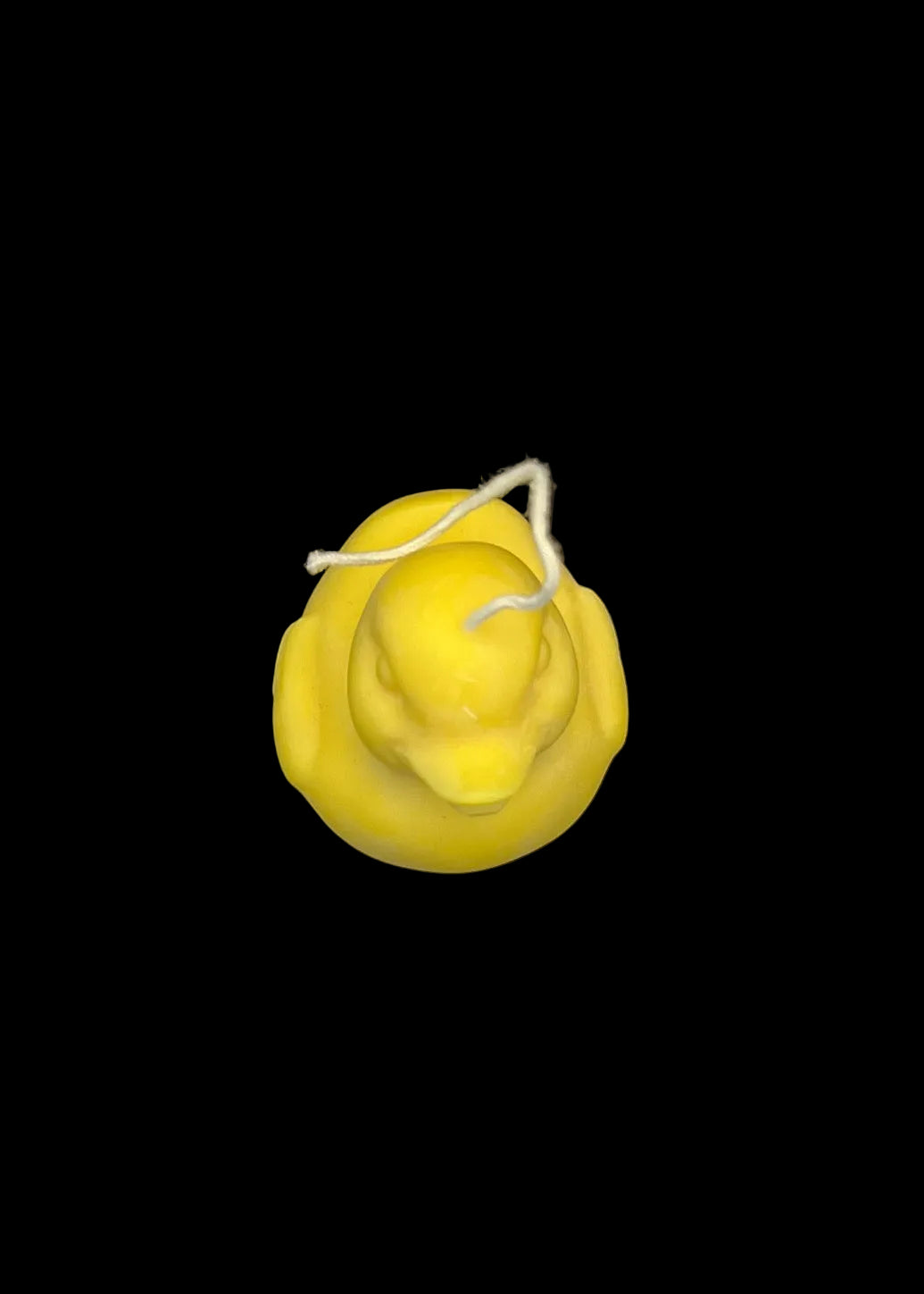 A small yellow duck-shaped candle with a white wick, photographed from above on a dark textured surface.