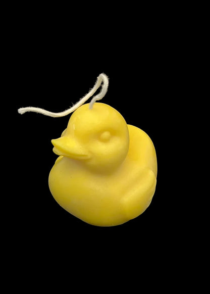 A small yellow duck-shaped candle with a white wick, photographed against a solid black background.
